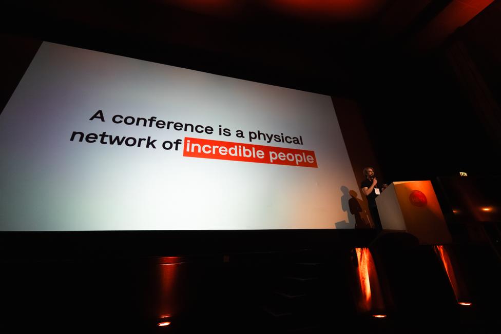 Josh Nesbitt on stage hosting All Day Hey!, beneath a slide reading 'A conference is a physical network of incredible people'